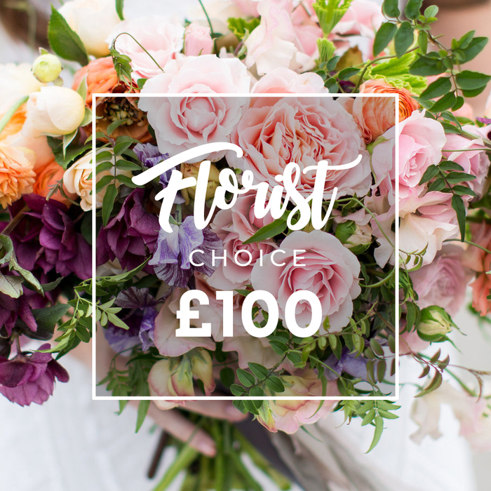 A rich, tactile bouquet is presented in this photograph with a clear artisan sensibility: the composition is anchored by several large, romantic garden roses in varying shades of soft pink, their ruffled centers creating a plush, voluminous focal point. Interwoven among them are deep plum-toned hellebore-like blossoms that provide shadow and sculptural contrast, while pale purple-and-white striped sweet peas float through the arrangement, adding a whimsical, airy texture. Coral and peach ranunculus-style flowers appear like rippling shells of satin, their tightly packed petals catching the light and offering warm undertones. Creamy white filler blooms and tiny unopened buds add glints of brightness, and a variety of green foliage - from wiry vines to fuller, matte leaves - shapes the bouquet into an organic, garden-harvest silhouette. Across the centre of the scene a thin white square frame overlays the blooms with understated clarity; within it an elegant script proclaims Florist Choice (with the secondary type in smaller capital letters) and a bold ?100 anchors the pricing information. At the bottom edge, a person's hands cradle the bundled stems, fingers visible against a softly blurred pale sleeve, suggesting careful handling and immediate readiness for presentation. The lighting is soft and natural, revealing each petal's texture and the slight sheen on leaves, evoking scent and tactile softness. This arrangement reads as a bespoke, premium option ideal for weddings, anniversaries, or as a thoughtful luxury gift, suitable for delivery around Epping - from the High Street to nearby Bell Common and the lanes that meet the forest.