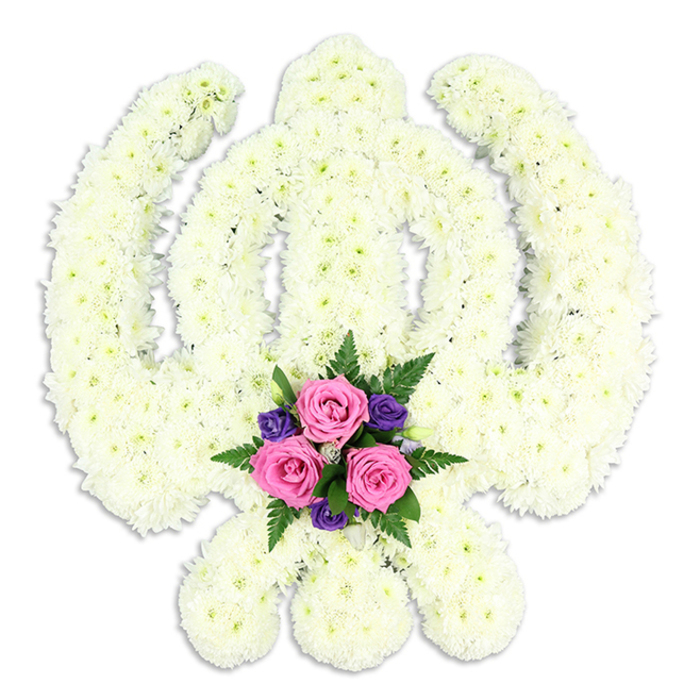 A striking Sikh Khanda funeral tribute is presented in a clean, white setting, allowing every crafted detail of the floral work to stand out clearly, much as it might on display in a calm chapel of rest serving families around Epping. The entire sacred symbol-central double-edged sword, circular chakra, and the symmetrical sweep of the two kirpans-is constructed from densely packed white chrysanthemums, chosen for their purity and longevity. Each bloom is set closely side by side, so the surface looks like a continuous field of creamy white, edged with soft, rounded contours rather than harsh lines. The petals form a fine, almost plush texture that suggests both comfort and devotion. At the base of the Khanda, where the lower points of the kirpans curve inward, a compact posy of colour provides a gentle yet striking contrast. Three medium-sized pink roses sit at the heart of this accent, their petals fresh and layered, catching the light with a subtle sheen. Around them, deep purple flowers-likely lisianthus, freesias, or similar dainty blooms-add a cooler, more contemplative note, while fronds of dark green fern and supporting foliage frame the cluster and soften its edges. The small accent bouquet is carefully placed so it does not overpower the Khanda, but rather brings a sense of personal love and remembrance, as though chosen by the family themselves. A faint shadow beneath the arrangement gives it depth and presence on the white background. This bespoke Sikh tribute would be fitting for funeral services and memorials across Epping, symbolising faith, honour, and eternal remembrance in a way that feels both traditional and tenderly individual.