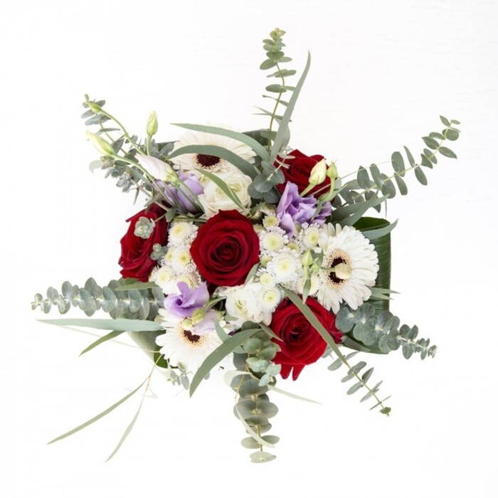 In the heart of Epping, where leafy lanes wind toward the ancient forest, this bouquet stands as a testament to refined local craftsmanship. The creamy gerberas, radiant with a subtle warmth, anchor the ensemble-their broad petals unfolding around espresso-brown centers that ground the bouquet with quiet dignity. Spiraled red roses nestle confidently amongst them, their deep velvet tones whispering affection and enduring bonds. Lisianthus in shades of pale lilac drift through the arrangement, some curled tight in hopeful bud, others unfurling softly, reminiscent of wildflowers glimpsed at the forest's edge near Bell Common. Flecks of ivory filler blossoms lend delicate fullness, imparting an airy grace. Intertwined throughout, eucalyptus leaves shimmer in silvery-green, brushing the bouquet with both fragrance and movement-like the gentle sway of Epping's wooded canopy in a morning breeze. Robust, dark green leaves contour the base, cradling the composition within a vibrant embrace. Set within a clear glass vase, the freshly cut stems glint beneath the water's surface, a visible reminder of the bouquet's just-gathered freshness and Flowers Epping's dedication to quality. The entire arrangement radiates a serene, welcoming spirit, its layered scents of rose and eucalyptus conjuring a sense of calm and connection-perfect for marking milestones, offering comfort, or making a new house in Epping truly feel like home.
