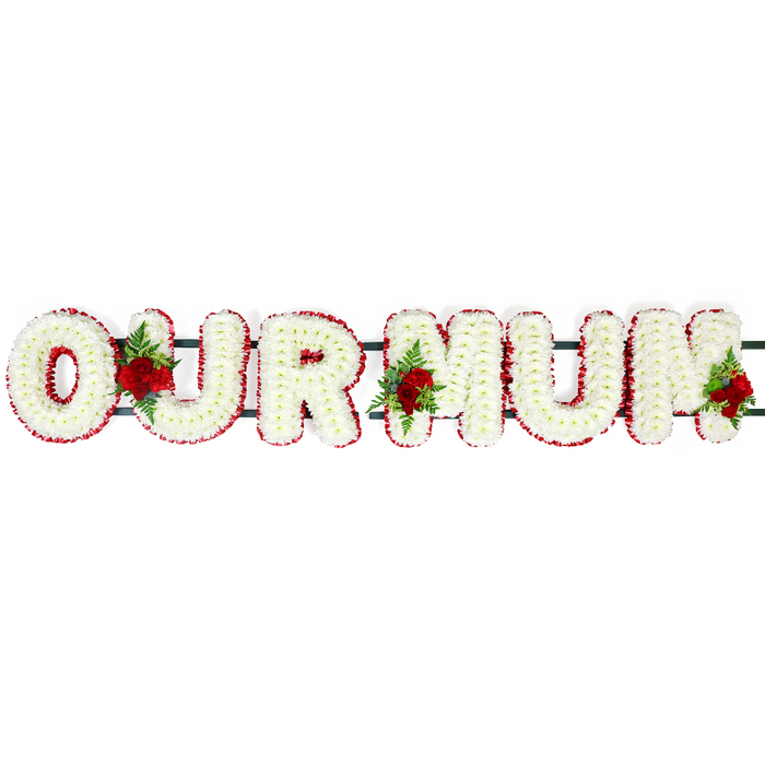 A lovingly crafted funeral letter tribute spelling out OUR MUM stretches across the frame, arranged in a horizontal line against a bright white, shadow-free background that makes the colours appear vivid and true. Each tall block letter is intricately covered in small white chrysanthemum heads, the blossoms carefully aligned so that no gaps of foam or frame are visible, giving the impression of soft, freshly fallen snow pressed into a perfect shape. Along the outer edge of each character runs a rich border of deep red spray carnations or similar small flowers, their ruffled petals forming a neat, continuous band that both defines and embraces each letter. Three striking clusters of fully opened red roses add depth and sentiment, nestled among the white blooms with their stems hidden, as if they have naturally grown from within the tribute. These rose groupings are dotted between the letters, accompanied by sprays of dark, glossy foliage and delicate fern, bringing an extra layer of texture and a fresh, leafy scent to the arrangement. Just behind the blooms, slim dark green bars connect the backs of the letters, suggesting a sturdy frame designed for safe transport and display at a funeral service or graveside committal in and around Epping. The whole piece feels composed and reverent, like something a family from a quiet street near Epping Station might choose to accompany their mum on her final journey. The restrained palette of white, red, and green carries a clear message of love, respect, and gratitude, forming a floral tribute that quietly holds a lifetime of memories within its simple words.