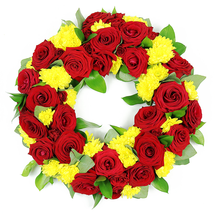 In this image, a striking circular funeral wreath is photographed against a clean, bright white background, allowing every bloom and leaf to be seen clearly. The wreath forms a complete ring with an open centre, carefully constructed from a dense mix of deep red roses and vivid yellow chrysanthemums that touch and overlap so there are no obvious gaps. The roses dominate the structure, their velvety petals arranged in classic spirals that move from tight inner whorls to gently unfurled outer edges. Shades range from a pure, romantic crimson to a richer burgundy, creating a layered effect that suggests depth and quiet intensity. Nestled between these roses are multiple clusters of small yellow chrysanthemums, possibly spray or button varieties, their many fine petals forming puffed, cushion-like blooms that look soft and almost feathery to the touch. The yellow introduces a bright, hopeful contrast to the more serious red, offering a sense of comfort akin to the gentle light that filters through the trees in Epping Forest. Around and beneath the flowers, lush foliage provides structure and balance. Broad, glossy green leaves-likely salal or ruscus-sit alongside softer, grey-green sprigs that resemble eucalyptus, giving the wreath a natural, woodland character. The greenery is woven carefully so it frames the flowers without overwhelming them, ensuring the ring feels both full and harmonious. The craftsmanship suggests the steady hand of a local Epping florist, accustomed to preparing respectful tributes for services at nearby churches, crematoria, and gravesides. Even lighting casts minimal shadow, emphasising the saturation of the reds and yellows and the fresh, healthy look of the leaves. The overall impression is of a dignified, heartfelt expression of love, remembrance, and gratitude.