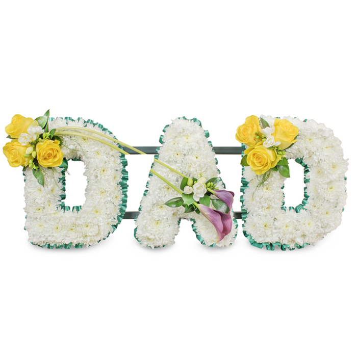 A striking floral memorial that spells out the word DAD in bold, three-dimensional letters, each carefully crafted from a dense bed of pure white spray chrysanthemums that form soft, rounded surfaces. The letters are neatly traced with a ruffled, dark green satin ribbon or foliage edge, which gives each character a defined silhouette against the white ground; slim, dark green support bars run horizontally behind the arrangement to anchor and connect the pieces into a unified display. On the upper left curve of the first D sits a bright cluster of cheerful yellow roses, their open faces catching imagined light, paired with tiny white freesias or gypsophila and fresh green leaves; several long, thin green stems extend upward and across, adding a graceful line. The central A is embellished at its lower diagonal with two elegant, deep purple calla lilies whose trumpet-shaped blooms offer a dignified, contemplative focal point, surrounded by subtle white accents and soft foliage. The final D mirrors the first with an equivalent cluster of sunny yellow roses and white fillers on its upper right curve, producing a balanced, symmetrical composition. Set against a plain white backdrop and finished with delicate greenery, the piece carries a gentle, clean fragrance and a palette of white, yellow, deep purple, and rich green. This arrangement is designed as a heartfelt funeral tribute or memorial for a beloved father, appropriate for services across Epping and the nearby parishes, reflecting respectful craftsmanship, floral expertise, and a quiet tenderness.