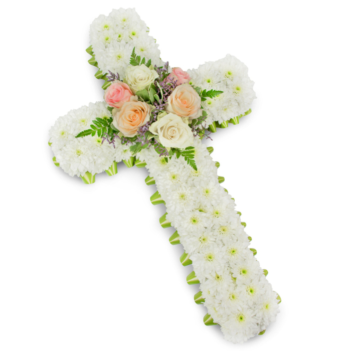 The image presents a refined Christian cross crafted entirely from fresh flowers, set against a clean white background with a subtle drop shadow that gives the arrangement depth, as though it has just been placed in a light-filled chapel near the heart of Epping. The cross's arms and central stem are thickly padded with neat, button-style white chrysanthemums, each bloom pressed closely to its neighbour so that the eye sees an uninterrupted expanse of snowy petals. This dense coverage creates a soft, quilt-like texture, suggesting comfort, purity, and the gentle stillness often associated with a memorial service. At the very centre of the cross, where the beams meet, a small cluster of luxury roses becomes the emotional focal point. Fully opened roses in shades of pale pink, warm peach, and creamy ivory nestle together, their layered petals curving outward like soft spirals. Interwoven among them are delicate fern fronds and tiny sprigs of lavender or light purple filler flowers, introducing hints of movement and a whisper of colour without overwhelming the design. Framing the entire piece is a narrow band of lime green ribbon, tucked neatly beneath the chrysanthemums so that just a slim edge of green outlines the cross. This bright yet tasteful border sharpens the silhouette and introduces a touch of fresh, springlike energy, reminiscent of the greenery lining the paths around Epping Forest. Overall, the arrangement feels reverent and carefully made, an ideal floral tribute for funerals, memorials, or graveside remembrances, conveying faith, respect, and enduring affection for a loved one.