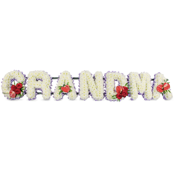 A quietly poignant sympathy tribute spells 'GRANDMA' in bold, capital letters, each letter entirely formed from densely packed white cushion chrysanthemums or closely related spray blooms, giving a plush, velvety texture that reads as both pure and comforting. Each character is trimmed with a subtle band of pale purple ribbon that creates a soft shadow at the edges and adds an understated hint of colour. Carefully placed clusters of vivid red flowers - classic roses and full carnations - provide striking visual punctuation at intervals across the word, while sculptural red anthurium lilies, with their unmistakable heart-like form, are married to the floral masses at the first 'A', the 'M', and the final 'A'. The sweeping 'G' is accented with a rich grouping of red roses and a variegated red-and-white calla lily, its elegant funnel shape nestling into the curve and introducing a refined contrast of pattern and line.

The letters are mounted on a discreet dark green support frame that keeps the presentation dignified and stable, the mechanics intentionally disguised to maintain the arrangement's solemn beauty. Speaking as a florist who has created remembrances for families across Epping - from St Margaret's Road to the thoroughfares near the Epping Ongar Railway - I imagine the tribute displayed at a wake or graveside, the cool, gentle scent of chrysanthemums and the deeper perfume of roses offering subtle comfort. This design is crafted to be legible from a distance yet intimate close-up, a respectful, personal memorial piece that conveys enduring love and grateful memory for a beloved grandmother.