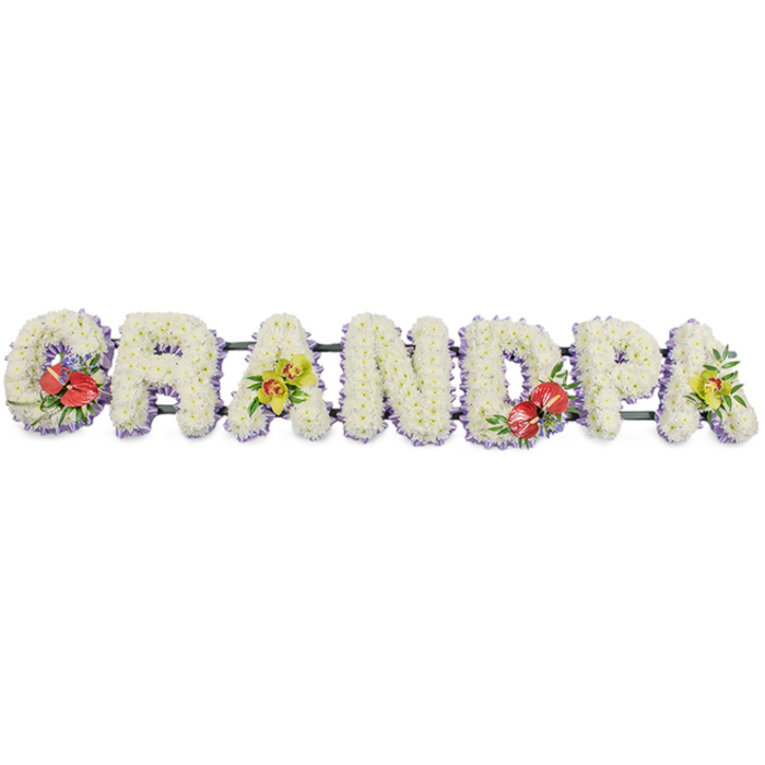 A beautifully composed sympathy tribute spells out GRANDPA in tall, substantial letters, arranged in a straight line against a plain white background so that every detail of the floral work is clearly visible. Each character is formed from masses of small, pristine white chrysanthemums, placed so closely together that no gaps can be seen, giving the surface a soft, almost quilted look. The cool white blossoms, with their delicate, feathery petals, convey serenity and respect, like quiet light filtering through trees on the edge of Epping Forest. Along the lower edge of each letter, a subtle trim of pale lavender ribbon adds a gentle, understated contrast and gives a neatly finished profile when viewed from the side. Dark green metal or wooden bars link the letters from behind, providing the strength needed for the tribute to rest securely on an easel or stand during a funeral service at a local Epping church or crematorium. Carefully placed accent sprays bring touches of colour and personality: the G and D hold compact arrangements of deep red anthuriums, their glossy, heart-shaped blooms catching the light, surrounded by dark green leaves and hints of fine filler. The first and last A are softened with clusters of yellow-green orchids, their petals elegant and slightly translucent, nestled into fresh foliage that introduces movement and grace. The finished piece feels thoughtful and bespoke, a personalised floral farewell for a beloved grandfather whose presence is deeply missed, yet warmly remembered by family and friends gathered nearby.