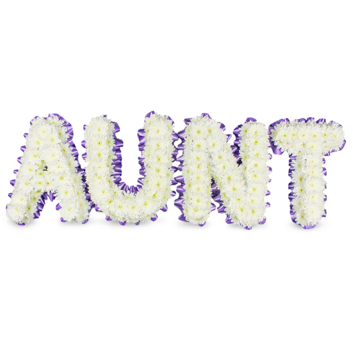 A meticulously arranged floral message reads AUNT in bold capitals, each letter densely packed with hundreds of small white spray chrysanthemums to form a soft, textured surface that feels almost cloudlike. The chrysanthemums' petals are tightly ruffled, producing a gentle relief across the letter faces, while occasional pale yellow centers appear like tiny, quiet suns tucked into the white. Around the perimeter of each letter, a deep purple satin ribbon has been carefully applied and slightly pleated to create a scalloped outline that contrasts with the blossoms and lends a refined silhouette against the plain white backdrop. The ribbon's satin finish picks up the ambient light-think the diffused daylight that filters across Epping High Street windows-adding a muted sheen and a sense of craftsmanship. Beneath each letter, faint grey shadows indicate the underlying letter frames and give the tribute a real-world solidity suitable for placement on a donation table at a memorial service or beside a casket. The overall composition conveys dignity, respect, and a personalized approach to remembrance; the white suggests purity and the purple trim signals thoughtful tribute. There is a clean, herbal-chrysanthemum scent that arises gently from the densely packed blooms, reinforcing the sense of calm. Designed with precision and heart, this arrangement is the sort of bespoke funeral flower families in Loughton and Debden might choose to honour a beloved aunt, offering a visible, tactile expression of love and farewell.