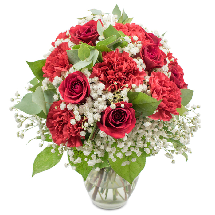 A beautifully rounded bouquet of red and white flowers stands in a simple clear glass vase, photographed against a bright white background that lets the rich colours and textures take centre stage. Deep red roses form the focal point, each bloom with tightly layered, velvety petals spiralling inward, like little symbols of romance and devotion. Interspersed generously among the roses are ruffled red carnations in the same vivid crimson shade, their densely layered petals adding volume and a lush, almost cloud-like softness to the overall shape. Throughout the bouquet, airy clusters of pure white baby's breath drift between the red blossoms, their countless tiny florets catching the light and softening the dramatic palette, creating a feeling of innocence and balance. Supporting this mix is an array of green foliage: dark, classic rose leaves provide a strong, glossy backdrop, while rounded eucalyptus leaves bring a cooler, silvery-green tone and a more relaxed, natural rhythm to the design. The stems are clearly visible through the transparent vase, set in clear water that reflects the clean, careful craftsmanship of a local Epping florist. Bright, studio-style lighting from above and in front enhances the contrast between the reds, whites, and greens, casting soft shadows that give the arrangement depth without overwhelming it. The bouquet's dome-like profile makes it ideal as a centerpiece on a dining table in a home near Epping High Street or as a welcoming display in a hallway close to Bell Common. With its timeless red-and-white colour story, the arrangement conveys love, admiration, and heartfelt congratulations, perfect for anniversaries, romantic surprises, or simply brightening a special evening at home.