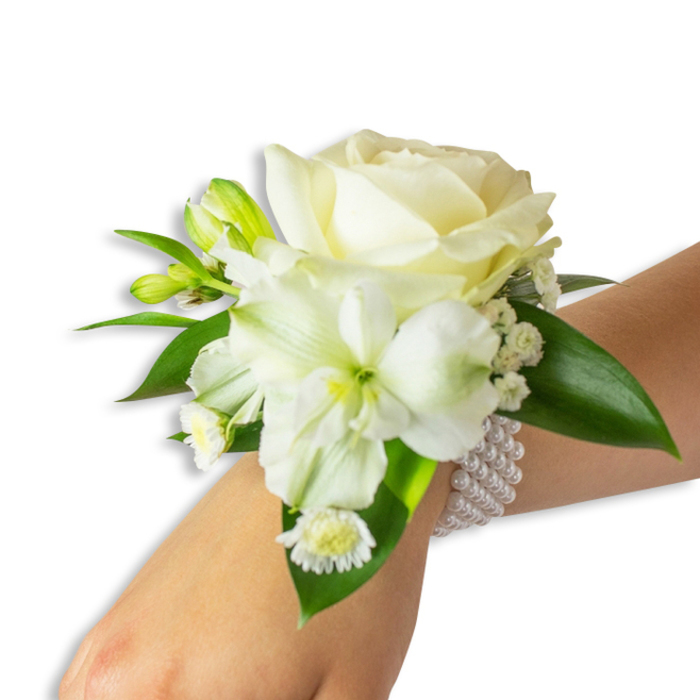 A refined floral wristlet displayed from a slightly overhead angle, the fair-skinned wrist angling in from the lower right so the arrangement reads clearly against a studio-white field. The centrepiece is a lush, creamy white rose, its petals unfolding with soft, velveteen texture and a hint of warmth in the ivory hue. Slightly below and to the left, a larger trumpet-shaped white bloom-possibly an airy alstroemeria-shows a delicate greenish-yellow throat that provides subtle contrast and dimensionality. Interwoven are several compact green buds, poised to open, and fine sprays of baby's breath that create a misty, lace-like backdrop around the principal blooms. Toward the lower portion of the cluster, a small white daisy-like blossom with a golden yellow eye punctuates the design with an innocent, almost playful note. Rich, glossy deep-green leaves frame the bouquet, their smooth surfaces and strong veins giving structure and weight to the soft whites. The piece is secured by a multi-strand pearl bracelet, strands of perfectly rounded white pearls forming an elasticised band that cradles the wrist and elevates the floristry into classic refinement. The overall impression is one of poised simplicity: tactile, fresh, and quietly celebratory. Imagine this worn during a summer wedding in Epping, or stepping out for photographs along the tree-lined lanes by the Epping Ongar Railway-an accessory that complements both formal gowns and the soft light of early evening, made with careful attention to balance, scent and lasting comfort.