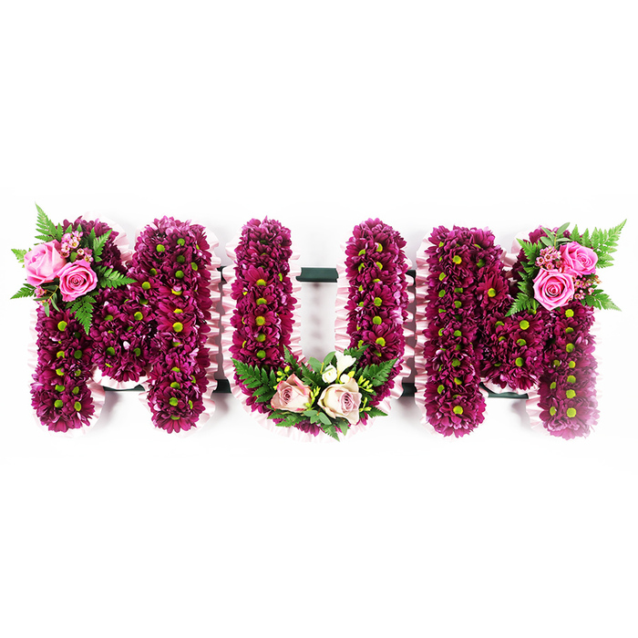 This image shows a heartfelt MUM funeral tribute, composed as three large floral letters arranged in a straight line against a spotless white backdrop. Each letter is meticulously built from a base of closely set magenta and deep purple spray chrysanthemums, their rounded petals overlapping to create a plush, almost quilted surface. The blooms are dotted with soft green centres that catch the light and lend a delicate brightness throughout the design. Along the sides of every letter, a pale pink ruffled ribbon is carefully pinned in place, tracing the contours with a gentle, scalloped edge that adds a handcrafted touch typical of bespoke arrangements made for families in Epping and nearby villages like Fyfield or Coopersale. The first M features a graceful floral accent at its top-left shoulder: fully open bright pink roses and smaller buds, cradled by fresh fern fronds and small leaves that arch slightly outward, as if offering a final embrace. The centre U carries a more tender decoration at its base, where soft blush-pink roses and creamy white blossoms, reminiscent of freesia or similar dainty flowers, curve softly along the inner shape, supported by lush green foliage. On the second M, a matching spray of rich pink roses and ferns adorns the top-right edge, creating a harmonious balance from side to side. The tribute feels both substantial and gentle, with its strong colour palette and soft textures working together. It is the kind of personalised MUM arrangement local families might place at Epping Forest Burial Park or a graveside service, conveying love, respect and enduring remembrance for a cherished mother.