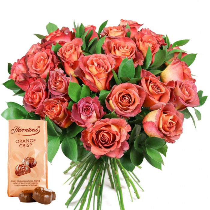 Dominating the composition is a lavish, round bouquet lush with open roses, its warmth and vibrancy heightened by the crisp, pure white background-a hallmark of refined Epping elegance. Expertly assembled by local florists attuned to the preferences of our town, the roses cascade from golden peach and soft cream at their centres, through rich gradations of coral, salmon, and deep rose at the petal edges. Many blooms display a nuanced ombre effect, recalling sunrise over Epping's verdant parks, while some remain tightly furled, waiting to unfold. Dark, glossy greenery, likely eucalyptus or ruscus, encircles and highlights the flowers, providing depth and a verdant freshness reminiscent of the local woodlands. The bouquet's neat stems peek from beneath, testifying to its hand-tied, artisanal preparation. In the foreground's lower left, a pristine Thorntons Orange Crisp chocolate pouch sits upright, its beige wrapping sharply printed with the brand's logo and bold lettering. Below, an enticing illustration promises the zesty orange-flavored truffles, with two unwrapped chocolates resting temptingly before the packet-their rounded, glossy coat inviting indulgence. Every element is designed for sensory pleasure and local giving; perfect for celebrating love, birthdays, or special milestones anywhere from Hemnall Street to Ivy Chimneys, this set radiates joyful sophistication and the care of true Epping craftsmanship.
