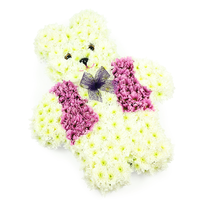 This image shows a teddy bear-shaped floral tribute, thoughtfully designed to convey comfort, innocence, and love, much like a cherished toy treasured by a child in Epping. The entire bear is constructed from clusters of creamy white chrysanthemums, arranged so closely together that they create a soft, velvety surface reminiscent of plush fabric. Its rounded head, gentle ears, and softly curved limbs are all carefully defined by the placement of the blooms, giving the figure a full and cuddly silhouette. At the centre of the face, two small, dark eyes are set amid the petals, with a neat black triangle forming the nose, lending the bear a peaceful, almost protective expression. A faint suggestion of a smile beneath the nose enhances its kind and consoling presence. Across the teddy's chest, a distinct waistcoat effect is created using rich pink and magenta chrysanthemums, grouped densely to form two panels that echo the look of a smart little jacket. Between these panels, at the neckline, rests an airy bow made of sheer purple netting, its soft, translucent layers adding an extra touch of detail and charm. The arrangement is photographed against a bright white backdrop, which allows the creamy tones, the deeper pinks, and the violet bow to stand out with clarity. This floral bear feels particularly suited for a child's funeral, a memorial near Epping Forest, or a tender remembrance service in one of the town's churches, offering a gentle floral embrace when words alone cannot express the depth of feeling. It could also bring sweetness and hope to christenings, naming ceremonies, or baby showers in the local area.