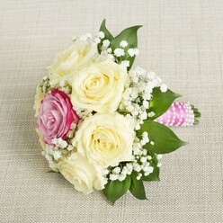 Imagine the delicate artistry of a small bouquet, carefully crafted by an Epping florist, resting softly on a pale fabric that feels like the first light on Cottis Lane. Ivory roses, their petals unfurling in creamy spirals, create a serene focal point suggestive of morning calm in the Epping Market Square. Nestled gently among them is one striking magenta-pink rose-a highlight capturing the wonder of springtime walks in Epping Forest. Cloud-like clusters of airy white baby's breath weave between the blooms, offering gentle contrast both in colour and texture. Deep, emerald green leaves peek from beneath, grounding the airy elegance with a richness reminiscent of fresh country greenery after rain. The stems are bound with glossy pink satin ribbon, lovingly finished with a spiral of glistening pearls-each touch lending a sense of modern celebration and timeless grace. The gentle glow of soft daylight caresses each petal, inviting thoughts of joyful weddings or special gatherings held in Epping's welcoming community halls. The understated floral arrangement speaks to craftsmanship shaped by years of local experience, with every detail expressing a balance of classic beauty and heartfelt emotion-perfect for conveying love and celebration in the heart of Epping.