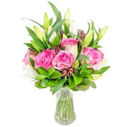 A carefully composed bouquet of luxurious deep-pink roses and awaiting white lily buds sits in a simple clear glass vase, arranged against a clean white background so every hue and petal detail is visible. The roses form the visual centre-large, fully opened blooms whose velvety petals layer from soft blush to rich fuchsia, lending the arrangement a sumptuous, tactile quality. Sprinkled among them are white lilies mostly in bud, their tapered shapes hinting at trumpet blooms to come and carrying the quiet, powdery perfume of early morning blossoms. Surrounding foliage varies from broad, glossy leaves that create bold, verdant planes to delicate, feathery sprigs that introduce movement and lightness; subtle touches of darker burgundy filler or small buds add contrast and textural interest. The vase's tapered profile and crystal-clear water make a neat grid of green stems visible, emphasising freshness and skilled tying. Photographed with bright, diffuse lighting, the bouquet's rounded silhouette reads both classic and contemporary-appropriate for Mother's Day, a romantic gesture, or to lift a living room corner. The mood is celebratory yet composed, evoking the unspoken care behind a thoughtfully made arrangement. Imagine this placed on an Epping coffee table near a window looking toward Epping Forest, filling the room with colour and a soft floral scent that feels like a small, persistent joy.