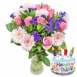 Captured in gentle daylight against a white background, this celebratory bouquet reads like a small festival of texture and pastel tone, perfect for a birthday gift in Epping. The arrangement rests in a simple clear glass vase with a modestly wider base so the stems and clear water are visible, reassuringly fresh. Dominating the composition are dozens of soft pink roses, their petals unfurling from palest blush to a warmer rose, lending a romantic fullness. Scattered between the roses are large pale-pink Gerbera daisies whose layered, radiating petals and subtle buttercream-yellow centres offer a cheerful, open contrast. Interspersed throughout are abundant clusters of deep purple filler - statice or limonium - that introduce a crisp, slightly papery texture and a striking colour punctuation. Glossy green leaves wrap the blooms, adding weight and a lived-in, garden-fresh feel. To the right-hand lower corner a cake-shaped foil 'Happy Birthday' balloon lifts the arrangement's spirit: predominantly white with a blue wavy icing border, colorful sprinkles in red, yellow, blue and green, and four striped candles in purple, red, orange and blue with yellow flame tips. The greeting is printed in playful multicoloured type and the small 'KALEIDOSCOPE' logo appears at the balloon's foot. As a local florist familiar with Epping - from the High Street to the edges of Epping Forest - I picture this set delivered with care, a bright, fragrant moment for a birthday table or bedside, its scent faintly sweet and its presence immediately celebratory. Flowers Epping can prepare similar bouquets for same-day collection or delivery around Station Road and nearby streets.