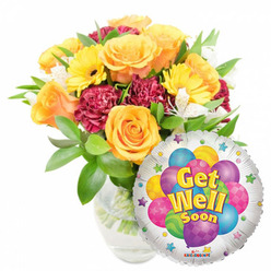 A sunny, compassionate 'Get Well Soon' display I often assemble at Flowers Epping, styled here against a plain white background for clear visual focus. The composition places a lush bouquet slightly left of centre in a clear glass vase, stems visible in clean water, while a round silver Mylar balloon nestles to the lower right and partially overlaps the flowers. The floral heart of the design features full, soft orange and deep yellow roses whose layered petals suggest warmth and gentle fragrance; bright yellow gerbera daisies contribute bold, sunlit faces; and dark maroon carnations bring ruffled substance and visual depth. White alstroemeria flicker through the bouquet like tiny, bright notes, adding lightness and delicate lines. The foliage is plentiful and varied - rich green leaves with glossy surfaces and subtle texture cradle each bloom and lift the arrangement's silhouette. The balloon's mirrored surface catches room light and carries a cheerful cluster of illustrated balloons in blue, purple, green, pink and yellow - some striped, some dotted - with the central message "Get Well Soon" in a friendly yellow-and-blue type and small starbursts decorating the edge; a tiny KALEIDOSCOPE logo appears along the bottom rim. Soft morning light sculpts the petals and metallic shine, creating an image that feels caring and hopeful. Prepared with neighbourhood deliveries in mind, this ensemble suits bedside cheer in local Epping homes near the High Street or collection after a stroll through Epping Forest.