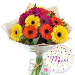 A colourful hand-tied bouquet of gerbera daisies is captured in a bright studio setting, its joyful hues instantly evoking celebration and affection. About a dozen large gerberas in glowing yellow, lively orange, and deep magenta are grouped closely together, each bloom perfectly circular with smooth, radiating petals and a dark central eye. The flowers sit at slightly different heights, creating a gentle dome shape that feels abundant yet relaxed, the way a local florist in Epping might prepare a gift for a family gathering near Theydon Bois or Coopersale. Rich green leaves weave among the flowers, softening the transitions between colours and lending a fresh, garden-picked impression. The stems are carefully aligned, then wrapped in a layer of rustic brown kraft paper that shows natural creases and folds, giving the bouquet a tactile, earthy charm. Over this, a sleek coat of clear cellophane encloses the stems, catching points of white highlight and subtly mirroring the bright petals. A length of natural twine is tied firmly around the base, the bow slightly off-centre in an intentionally casual yet thoughtful finish. The arrangement stands in a tall, slim glass vase filled with clean water, every straight green stem clearly visible through the transparent sides. To the lower right of the flowers, a single round foil balloon adds a personal touch. It is white, scattered with gold and pink confetti dots and tiny heart motifs, and bears the affectionate message "best Mum" in sweeping pink cursive across the centre. The entire composition radiates warmth, gratitude, and pride, perfectly suited to be delivered across Epping as a Mother's Day surprise or a heartfelt thank-you to a much-loved mum.