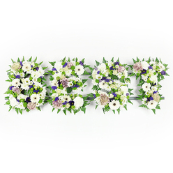 This heartfelt floral tribute spells the word "DAD" in a broad, reassuring tapestry of whites, purples and greens, arranged with the care of a local florist and captured against a bright white background. Each capital letter is densely packed with soft ivory gerberas, billowy chrysanthemums and creamy coffee roses that read as gentle and familiar, lively yet serene. Small clusters of violet statice and pale mauve carnations are woven through the white blooms, offering tender pinpricks of colour that suggest warmth and affectionate remembrance rather than loud celebration. A fringe of vibrant fern leaves traces the outline of every letter, their crisp lobes creating movement and a green frame that gives the tribute a living, breathing quality. The blooms sit on a subtle dark grey base that shapes the letters; in the soft studio lighting you can see tiny shadows that add depth and clarity to each curve and edge. Texturally, the piece balances smooth rose petals, the feathery softness of carnations, and the sculpted faces of gerberas, producing a comforting bouquet that feels both substantial and intimate. Imagine the faint fragrance of fresh roses mingling with green, earthy notes from the foliage-simple sensory comforts at a difficult moment. Designed for a funeral or memorial service in Epping or delivered to a chapel near the High Street, this arrangement is the kind of personalised tribute Flowers Epping prepares with care: a tangible, floral embrace when families seek to honour a father's memory with dignity and love.