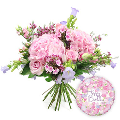 Against a pure white backdrop, a lavish, hand-tied birthday bouquet is displayed with the kind of balance and care you'd expect from an experienced florist just off Epping High Street. The arrangement is dominated by sumptuous blush pink hydrangeas, each head rounded and full, their overlapping petals giving the impression of soft fabric or billowing clouds. Nestled closely among them are soft pink roses, some fully open with their classic spiral centres on show, others still partially closed, adding a sense of gentle anticipation as they continue to bloom over the coming days. Threaded through the pinks are dainty clusters of magenta-toned waxflower, or similar tiny, cup-shaped blooms, whose deeper colour and fine texture create a lively, confetti-like effect. Rising in between are graceful spires of campanula, their bell-shaped flowers in shades of lavender and light periwinkle blue lifting the eye upward and lending the bouquet a playful, almost woodland charm reminiscent of walks through Epping Forest in late spring. A generous collar of fresh greenery surrounds the flowers: some leaves broad and deep green, others slender and more feathery, all contributing to a just-picked garden feel. At the base, the gathered stems are clearly visible, confirming this as a true hand-tied design, ready to pop straight into a vase on a birthday table in Epping or nearby Theydon Bois. To the right side of the flowers, a round foil balloon with a soft floral print glints slightly, its surface covered in small roses and buds that echo the bouquet's palette. Across its centre, in sweeping purple script, the words "Happy Birthday" are written, turning this image into a complete, heartfelt birthday gift moment rather than just a bouquet.