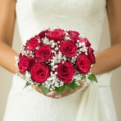 Overflowing with classic romance and shaped by the artistry of a true local florist, this wedding bouquet radiates with passion and poise. Close up, the vibrant dome of velvety red roses commands attention-the petals layered tightly, each bloom at a different stage, creating depth and a sense of unfolding promise. Interspersed among the roses, pure white gypsophila dances lightly, its tiny blossoms giving texture, softness, and the gentle airiness so loved in bridal bouquets across Epping. The stems are cradled by manicured hands, positioned just above the waist of a gown composed of intricate, softly textured fabric-perhaps inspired by the quiet grace of traditional ceremonies at Epping's local churches. Bright green leaves emerge subtly at the bouquet's base, their freshness recalling a stroll through the leafy lanes of town. The subtly blurred, cream-toned background ensures nothing distracts from the artistry and joy carried within the flowers and the bride's elegant attire. This bouquet, expertly arranged by Flowers Epping, embodies the eternal romance and sense of new beginnings that wedding couples seek, its rich fragrance and balanced composition a testament to both love and skilled local craftsmanship.