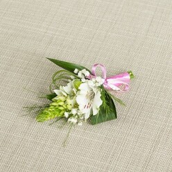 A refined floral boutonniere is arranged with meticulous care on a light beige, linen-like fabric, whose subtle weave gives a warm, natural backdrop that allows each botanical element to be clearly seen. At the centre is a pristine white alstroemeria, its petals slightly ruffled at the edges and marked with delicate reddish-brown streaks that draw the eye into the flower's open throat, where pale stamens stand poised. To one side, a striking column of vibrant lime-green buds rises like a miniature spire, each tiny bud fitting closely against the next, offering a bold, architectural contrast to the softness of the lily. Threaded among these focal points are airy sprigs of white baby's breath, their minuscule blossoms clustered like stars, bringing a sense of lightness and romance. Broad, dark green, spear-shaped leaves provide a sturdy base, while slender, grass-like fronds arc gently outward, giving the design a sense of flow and organic movement. The stems are gathered together and finished with a glossy pink satin ribbon, tied into a tidy, compact bow that adds a playful yet sophisticated note of colour. The even, diffused lighting captures the freshness of the flowers and the gentle sheen of the ribbon without casting hard shadows, creating a calm and elegant mood. This boutonniere feels ideal for a groom or prom guest heading out from Epping Station or celebrating near Epping Forest, a small but meaningful flourish that reflects the quiet beauty and thoughtful craftsmanship often found in local arrangements.