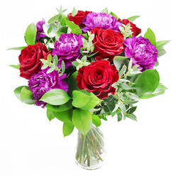 This bouquet presents itself like a confident guest arriving at a celebration in Epping, dressed in rich reds and regal purples. At its heart, luxurious red roses open wide, each bloom cupped with layers of velvety petals that spiral towards a dark, passionate centre. Nestled among them, plush purple peonies unfold in generous, ruffled spheres, their soft, clouded texture offering a graceful counterpoint to the more defined rose petals. A generous frame of greenery surrounds and supports the flowers: broad, polished leaves add depth, while slender stems of eucalyptus thread through the design, introducing cool, silvery-green tones and a sense of gentle movement. The foliage rises and falls around the blooms, giving the arrangement a natural, garden-like feel, as if it might have been gathered from a hidden corner near Epping Forest Countrycare trails. All of this rests in a simple, cylindrical glass vase, its transparency revealing the neatly trimmed stems crossing and converging in the water. Light glances off the vase and across the petals, making the reds seem to glow and the purples take on a soft, almost velvety sheen. In the imagination, the scent is a blend of classic rose sweetness and the crisp, invigorating aroma of freshly cut greenery. This is the kind of bouquet that seems at home on a dining table in a house near Bower Hill or as a dramatic centrepiece for a romantic dinner just off Station Road, perfect for commemorating an engagement, marking a special birthday, or lifting the mood of a room with a confident, heartfelt gesture.
