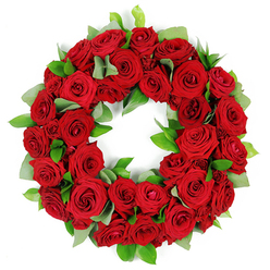 On a quiet morning in Epping, this wreath feels like a memory you hold close. A circular arrangement of dozens of deep red roses sits against a clean white backdrop, each bloom in varying stages-from tightly furled buds that promise tomorrow's joy to petals that have opened into velvety crescents, giving the ring a living, breathing texture. The red is lush and saturated, a rich signature of love and enduring respect, while deliberate pockets of green foliage-broad, matte leaves reminiscent of eucalyptus and narrower, glossy ruscus-thread through the roses, providing contrast and a sense of fresh, field-grown vitality. The ring is perfectly formed, an unbroken circle that carries the symbolism of remembrance and continuity, the composition balanced as if measured by a careful hand of a local artisan. Light falls with a soft precision, caressing the velvet of each petal and bringing out subtle shading from cranberry to ruby, so the arrangement glows without shouting. In Epping, such a wreath is a common messenger for funerals, memorial services, or anniversaries-a dignified tribute that speaks of loss accepted with grace and of lives well loved. It's the kind of piece that sits respectfully in a chapel, on a church altar, or at a family graveside, yet also easily serves as a heartfelt display at a funeral director's viewing room. Created by a dedicated local florist, it embodies the care, freshness, and craftsmanship you'd expect from Flowers Epping, with a quiet confidence that comfort can be found in colour and form.