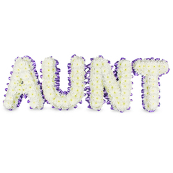 As a florist who often works with families across Epping and the surrounding villages, I describe this memorial as a carefully constructed message of love: the word AUNT formed in strong, uppercase letters, each letter densely composed of small, immaculate white spray chrysanthemums. The flowers are chosen for their long-lasting freshness and their gentle, ruffled texture; up close you can see pale yellow eye centers in some blooms, adding tiny points of warmth like memories catching light. A rich purple satin ribbon is hand-pinned around each letter's perimeter, the ribbon slightly pleated so it sits as a dainty, scalloped edge that both frames and protects the blooms. The contrast between the cool white petals and the warm purple trim reads as reverence balanced with tenderness. Subtle grey shadows beneath each letter hint at the solid, three-dimensional letter frames and give the tribute presence when placed on a chapel floor or service table. The scent is faintly green and fresh, with a clean chrysanthemum note that is never overpowering. I imagine delivering this tribute from Flowers Epping to a funeral service near Epping tube or to a wake at a village hall in Theydon Bois-a dignified, personal emblem that speaks of gratitude and remembrance. The overall effect is steady and comforting, created to honour a cherished aunt with dignity and floral craftsmanship that supports grieving families.