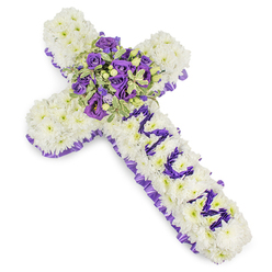 Presented on a stark white background to emphasise its precise craftsmanship, this cross-shaped sympathy tribute is built from countless white chrysanthemum blooms that create a seamless, cushion-like surface of purity and repose. The chrysanthemums are tightly placed so the cross reads as a unified whole rather than a collection of stems, giving the design solidity and a tactile softness that invites a gentle touch. Framing the piece, a ruffled purple satin ribbon traces the outer edge in a steady band of colour, the rich hue bringing an air of solemn elegance to the overall composition.

At the focal point, a compact but abundant central spray gathers deep violet and lavender roses with pale purple lisianthus, the roses' denser petals contrasting with the lisianthus' ruffled shapes to create depth and movement. Sprigs of variegated foliage-leaves with pale margins and darker centres-are woven through the cluster, adding light, structural highlights and a sense of fresh greenery; occasional small green berries introduce a subtle textural counterpoint. The vertical arm bears the word "MUM" spelled in smaller purple flower heads, the lettering deliberate and legible against the white field to make the sentiment unmistakable.

As a local florist familiar with Epping High Street and quieter corners near Epping Forest, I picture this design placed by a church door or on a graveside; it reads as a respectful, consoling piece. There is an understated fragrance and a calming palette that together offer solace while honouring a cherished life. Flowers Epping prepares such tributes for memorial services across Station Road and the surrounding community, always mindful of tenderness and detail.