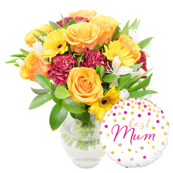 This image shows a carefully balanced bouquet in a clear glass vase, arranged to convey warmth and celebration with a soft, natural glow. Dominant peach-orange and golden yellow roses form the heart of the display, their petals layered in spirals that seem to unfold with each glance. Interspersed are vivid yellow gerbera daisies, their flat faces and dark centers throwing cheerful contrast against the richer tones. Deep maroon carnations introduce a plush, textured richness, their ruffled edges creating pockets of shadow that emphasise the brighter blooms. Slender white alstroemeria lilies with subtle speckles provide a delicate, airy punctuation throughout, while abundant glossy greenery-broad leaves and fine sprigs-wraps the bouquet in a verdant embrace. The clear vase shows clean water and trimmed stems, a visual detail that signals freshness and thoughtful handling.

Positioned to the bottom right and overlapping the lower flowers, a glossy round foil balloon completes the gift set. The balloon's white field is sprinkled with gold and hot-pink confetti-like dots and tiny hearts, with the phrase "best Mum" scripted across the centre in flowing fuchsia lettering, a sweet and direct message for Mother's Day or a birthday. The composition is luminous and tactile, like a present chosen after visiting local Epping markets or a favourite cafe on the High Street-calm, sincere, and designed to brighten a mother's morning.