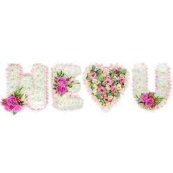 Seen from a gentle frontal angle on a brilliant white field, this bespoke memorial piece spells out H E (heart) U with the quiet authority of classic floristry. The letters H, E and U are each formed from tightly clustered white chrysanthemums, their tiny petals creating a soft, cloud-like surface that reads both serene and substantial. A delicate blush-pink satin ribbon frames every letter and the heart, its subtle ruffle giving the whole composition a ribbon-tied keepsake feel. Strategically placed clusters of intense fuchsia roses punctuate the white letters - two roses at the stem of the H, a trio resting on the E's middle bar, and a paired accent tucked into the inside curve of the U - each set accompanied by deep green foliage and small reddish berries which lend depth and a natural heartbeat to the design. The central heart diverges from the strict white of the letters, assembled from an abundant mix of soft pink carnations, blush lisianthus or miniature roses, and pale green eucalyptus that together create a cushioned, romantic centrepiece. The mixture of textures - the crisp chrysanthemum field, the velvety rose petals, the airy eucalyptus sprigs - invites both sight and scent to memory. The arrangement's mood is tender and reverent, suitable for a funeral or a commemorative display, and reflects the kind of careful work our local team is asked to create for families across Epping, from High Street wakes to services around Epping Forest.