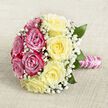 Set against a softly woven, oatmeal-coloured fabric, this hand-tied bouquet is captured from a gentle overhead angle, revealing its perfectly rounded form and thoughtful balance of colour. On one side, rich fuchsia and magenta-pink roses are clustered closely together, their petals unfurling in generous spirals that suggest fullness, passion, and celebration. Mirroring them, the opposite half is composed of creamy pale yellow roses, each bloom opening into a soft swirl of buttery petals that feel calm and reassuring, like early morning light over Epping Forest. Tiny white baby's breath is threaded throughout both halves, creating a lace-like veil that softens the transitions and adds an airy, almost dreamlike texture. A few deep green leaves emerge between the blossoms, bringing a natural freshness and hinting at the stems bound firmly beneath. The handle is wrapped in lustrous pink satin ribbon, smooth and slightly reflective, with a fine strand of white pearls twined around it in an elegant spiral, as if echoing the curves of the rose petals. Resting on the neutral linen, the bouquet appears ready to be lifted for a bridal portrait on Epping High Street or carried into a quiet registry office ceremony. There is a sense of gentle fragrance and quiet excitement, as though this arrangement has been created for a bride or partner who cherishes classic romance with a modern twist. Every detail feels intentional, from colour placement to texture, showcasing the careful artistry of a florist used to designing for intimate weddings and anniversaries across the Epping area.