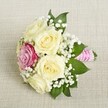 An exquisitely arranged small bouquet, thoughtfully placed on a softly woven, beige linen surface, reflects the refined style found at weddings across Epping. Five creamy white and pale yellow roses, their petals lush and unfurled, form the bouquet's gentle heart. Tucked slightly off-centre, a striking magenta-pink rose adds a dash of joyful colour, reminiscent of Epping's vibrant flower stalls on High Street. Wispy tufts of white gypsophila are nestled among the roses, introducing a classic, feather-light texture. Glossy, deep green leaves frame the flowers and add natural contrast, echoing the serenity of Epping's forest surroundings. The stems are expertly wrapped in textured pink satin ribbon that catches the light, accented with a spiralling strand of luminous pearls-a sophisticated touch characteristic of Flowers Epping's craftsmanship. Soft, natural lighting gently illuminates the arrangement, highlighting the intricate curves of each petal and the fresh, crisp greenery. Meant for weddings, anniversaries, or intimate gatherings, this bouquet beautifully conveys themes of romance and new beginnings-you can almost sense the subtle scent of roses drifting on the gentle Epping breeze.
