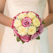A hand-tied bridal bouquet brimming with creamy white and blush-toned roses seems to glow softly, as though lit by the pale daylight filtering over Epping's Market Place. At first glance the shape is perfectly rounded and domed, with no harsh angles-just a smooth, cloud-like cluster of blooms held close together. Creamy ivory roses form the main body of the arrangement, their petals thick and silky, folding over one another in gentle curves. Between them, blush-pink and deeper magenta roses are threaded like whispered accents of colour, giving depth and romance without overwhelming the calm palette. Tiny clusters of gypsophila-baby's breath-scatter through the bouquet like lacework, softening the transitions between roses and adding flecks of bright white that catch the light. A few neat, deep green leaves sit low and discreet around the base, offering a cool, natural contrast to the warmth of the petals. The bouquet looks luxuriously full yet still delicate, as if it would rest lightly against a lace bridal gown or satin dress. You can almost sense the fragrance: a gentle, familiar rose perfume mingled with a fresh, dewy sweetness, like the first blossoms opening in gardens across Epping in late spring. The overall impression is of poise and inner calm, the kind of bouquet a bride might carry from a quiet home on the outskirts of Epping, through tree-lined streets, and into a ceremony filled with shared vows, soft music, and unspoken promises for the years ahead.
