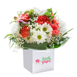 Soft cheer and lively charm come together in this stunning bouquet, reminiscent of a joyful spring morning in Epping. Coral, peach, and vivid red carnations form the lush heart of the arrangement, their abundance of ruffled petals inviting both touch and admiration. Snow-white daisies punctuated by bright, almost zesty green centers bring brightness and a sunlit innocence, recalling the wildflowers seen along Epping's local walking trails. Wisps of delicate white baby's breath drift between the main blooms, lending a gentle cloud-like textural contrast that softens the overall palette. On the upper left edge, hints of tightly closed, purple-brushed buds add an unexpected dash of depth and elegance. Broad, glossy green leaves wrap the bouquet in a verdant embrace, providing structure much like the shaded paths beneath the Forest's trees. All flowers nestle upright within a crisp square white gift bag, complete with sturdy ribbon handles: perfect for gifting on special days or simply to brighten a neighbour's doorstep in Epping. Every element is professionally arranged and showcased against a spotless white background, allowing the bouquet's freshness and positive energy to shine through. This arrangement would surely bring smiles, marking birthdays, anniversaries, or thoughtful moments with local warmth and expert care.