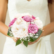 A romantic bridal bouquet brimming with creamy peonies, pink and lavender roses, and delicate gypsophila rests in the bride's hands, echoing the calm, unhurried charm of a wedding morning in Epping. At the heart of the arrangement, the peonies glow in shades of ivory and soft cream, their petals unfolding in plush, rounded layers that look as though they have been gently fluffed by hand. They feel effortless and serene, each bloom reminiscent of the soft clouds that sometimes hang above Epping Station on an early spring day. Intertwined with them, roses in muted dusty pink and gentle violet tones introduce warmth and subtle movement; some rosebuds are still tight and shy, while others are just starting to unfurl, suggesting the unfolding story of the couple's day. Wisps of gypsophila peep out between the larger flowers like tiny stars, lending an airy, bridal lightness that softens the whole design. Surrounding the blooms, glossy green leaves form a natural cradle, curving protectively around the bouquet and making the pastel colours appear even more luminous. The bouquet is carefully hand-tied and compact, designed to sit comfortably against the bride's dress as she walks through local venues, from historic churches near Epping Forest to intimate celebrations in family gardens. There is a tranquil balance to the composition, as if every flower has been placed with quiet intention by an experienced Epping florist who understands how local brides like their bouquets to feel-elegant, personal, and utterly romantic. The gentle play of light on the petals, the imagined soft fragrance, and the thoughtful mix of textures combine to create a piece that seems to murmur of harmony, love, and grace, ready to be captured forever in wedding photographs taken along Epping's tree-lined lanes.