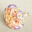 A stunning and meticulously arranged bouquet rests atop a softly textured, cream linen evoking Epping's peaceful charm. The focus is on plush, open peach and pale apricot roses, their petals hinting at spring orchard blossoms and gentle sunsets over Epping Forest. Nestled between these roses are elegant white lisianthus, each petal's edge touched with a lively violet hue, creating a playful and modern twist that stands out against the classic beauty of the roses. Ethereal sprigs of baby's breath meander throughout the bouquet, lending a cloud-like delicacy and nostalgic freshness, much like the seasonal wildflowers seen on local walks near Theydon Grove. The bouquet's overall shape is compact and rounded-a studied harmony of peach, ivory, soft lavender, and pure white, complemented by a tailored wrap of peach-pink satin ribbon, finished with a scattering of white pearl beads. This thoughtful detail ensures the bouquet is as comfortable to hold as it is elegant to behold, suited not only for timeless wedding processions at St. John's but also as a refined centrepiece for engagements or bridal teas hosted in Epping's welcoming homes. Every element, from the floral selection to the careful binding, tells a story of local artistry, joyful celebration, and heartfelt emotion, making it a perfect inspiration for anyone seeking romantic, contemporary wedding flowers in the heart of Epping.