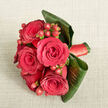 This image shows a richly detailed, hand-tied bouquet photographed from above, resting on a pale beige fabric that looks like softly crumpled linen, similar to the relaxed textures you might see in an Epping café near the station. The flowers themselves form a close, rounded cluster dominated by deep red roses, about five or six in full bloom, their petals unfurling in perfect spirals that feel both classic and intensely romantic. Tucked between the blooms are tight clusters of small, spherical red hypericum berries, smooth and glossy, adding a slightly lighter, almost orange-red accent that catches the soft light and introduces gentle movement to the eye. Enveloping the base of the bouquet, wide, dark green leaves are carefully wrapped and curled, creating an elegant frame that hints at tropical foliage while keeping the design compact, ideal for a wedding bouquet or an anniversary gift delivered to a home near Bell Common. Around the stems, a coordinating deep red satin ribbon is neatly wound, its polished sheen appearing just at the edge of the leaves, reinforcing the sense of craftsmanship and attention to detail. The lighting is calm and diffused, revealing the velvety texture of the petals, the waxy shine of the berries, and the subtle veins of the leaves without distraction. The bouquet feels intimate and passionate, a piece that could be carried down the aisle at a small Epping church ceremony or presented as a thoughtful romantic gesture, filling the room with the quiet promise of enduring love.