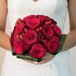 A sumptuous bridal bouquet takes centre stage in this evocative, close-up scene-its abundance of velvety, crimson roses glowing with deep emotion. Locally grown foliage and a collar of broad, glossy leaves anchor the arrangement, reminiscent of the fresh greenery found just steps from Epping's Monday market. Interspersed among the roses, radiant clusters of red hypericum berries add a jewel-like charm, their glossy orbs bringing a spirited contrast to the blooms. The bride, dressed in classic white with delicate lace accents, gently supports the bouquet with hands that speak of careful anticipation. Sunlight drifts through a softly blurred background, bathing the bouquet in warmth and amplifying the plush textures and rich tones that have made Flowers Epping renowned across the area. The bouquet's scent seems to linger in the air, mingling sweetness and earthiness-an unspoken echo of shared promises and the vibrant, joyous spirit of an Epping wedding morning. This arrangement brims with romance and tradition, perfectly suited for bridal features, wedding day captures, or those treasuring the heartfelt symbolism of red roses in the local community.