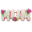 A thoughtfully composed standing tribute spelling MUM in large block letters, photographed against a clean white background so every detail reads clearly. Each letter is built from densely packed, pristine white chrysanthemums whose small, feathery heads give the letters a soft, pillowed surface; the overall effect is cool, pure and quietly dignified. The outer edges of each letter are finished with a ruffled pale pink ribbon trim that softens the silhouette and introduces a warm, comforting tone against the white blooms. A discrete dark green support frame is visible between the letters, the kind of practical structure florists use to keep a memorial piece upright at a chapel or graveside. Three vivid accent posies punctuate the design: the first M bears a tight cluster of rich fuchsia-pink roses and glossy fern-like foliage with pinpricks of coral-red hypericum berries tucked in; the U carries a matching arrangement nestled into its base curve; and the final M repeats the same pink roses, greenery and berries at its upper right. Textures move from the fine chrysanthemum spray to the velvety rose petals and the shiny, tactile berries, while the greenery adds a cooling, slightly resinous scent. This composition reads as a personal, mother-focused memorial - quiet yet affectionate - suited to a wake, church service or a graveside farewell. As a local florist familiar with Epping's gentle churchyards and the hush of Epping Forest on a subdued morning, I picture this piece standing near St John's or at a family home on High Street, where its colours and scent offer a calm, reassuring presence for those saying goodbye.