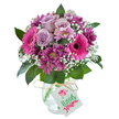 A radiant bouquet bursts with a vivid palette of fuchsia pink, soft lavender purple, and luscious magenta, showcased against a bright, pristine white backdrop-an image that conjures the fresh, contemporary sensibilities of Epping's thriving floral scene. Dominant in the arrangement are exuberant hot pink gerbera daisies, each sporting a signature dark centre, surrounded by clusters of gently unfolding pale lavender roses that infuse the composition with understated elegance reminiscent of early blooms in Epping's garden squares. Interwoven through the bouquet, smaller deep plum and magenta chrysanthemums add a richness and layered visual texture, their fine petals echoing the intricate beauty of wildflowers found along Theydon Road. Delicate sprays of white baby's breath and hints of lush green foliage create a natural frame and a sense of lightness, like the cool air filtering through the historic trees nearby. Every stem is carefully gathered in a clear glass vase, notable for its soft rounded shape and distinctive crackled finish-lending the piece an artisan, hand-touched character. The neck is simply adorned with a strand of natural raffia, from which hangs a celebratory white gift tag, cheerfully printed with 'Happy Birthday' in lively pink and green typeface and a petite flower motif. Designed with the festive occasions of Epping in mind-birthdays, thank-yous, anniversaries-this bouquet is a testament to the joyful artistry and expertise found in the heart of the community, bringing local colour and heartfelt emotion to every gesture of giving.