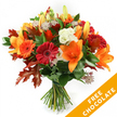 Against a pristine white background, a hand-tied bouquet stands upright like a small celebration of autumn light. Large orange lilies with trumpet-shaped blooms and visible stamens take centre stage, their waxy petals catching a soft, studio glow. Around them, ruby-red and bright-orange Gerbera daisies smile with dense, circular petals, while clusters of creamy white Lisianthus with ruffled edges add a crisp, almost cool contrast. Small, star-like Astrantia with purple-pink centres peek through, their intricate heads lending a delicate, lacy texture against the bolder blooms. Deep green leaves-likely ruscus or salal-form a glossy, verdant base, and the composition is punctuated by deeply lobed oak leaves in burnt orange and reddish-brown that immediately read as autumn foliage. The stems are neatly gathered and secured with a dark twine or raffia, the knot visible and slightly rustic, affirming the traditional hand-tied style.

The bouquet feels tactile and fragrant: the smooth, satiny petals of the lilies, the firm, velvety discs of the gerberas, and the papery crispness of the oak leaves combine into a warm, seasonal scent you can almost imagine. This arrangement is ideal for saying thank you, marking a birthday in late October, or bringing autumn cheer to a home on Epping High Street or after a walk through Epping Forest. In the lower right corner of the image a bright orange diagonal banner overlays the scene, boldly reading FREE CHOCOLATE in white capital letters-an eye-catching promotional detail included with the product image. The overall effect is expertly composed, warm, and welcoming, evoking a crisp, golden autumn afternoon in Epping.
