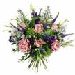 Captured against a pure white backdrop, this elegant bouquet glows with the soft romance of pinks and purples, composed with the assurance of a florist who understands both seasonal flowers and the tastes of Epping locals. At its centre, plush roses in gentle pastel pink and mauve unfurl in layers, some still slightly closed and others opening into full, cupped blooms that reveal subtle shifts in colour from deeper, rosy hearts to paler, almost creamy outer petals. Nestled among them, large ruffled carnations in dusty blush and muted mauve add depth and a delightfully frilly texture, like soft fabric gathering in folds. Rising through this softness are slim, tapering spikes of deep violet-blue Veronica, giving the arrangement graceful height and a slightly wilder, garden-grown feel, reminiscent of borders in well-tended Epping gardens. Scattered around these are clusters of lilac and periwinkle aster-like flowers, each tiny bloom with a distinct yellow centre, bringing a light, airy movement to the design. Touches of richer purple lisianthus tuck into the composition, adding pockets of velvety colour. The foliage has been chosen with equal care: cool, silvery eucalyptus leaves, more traditional green stems, and bursts of vivid lime-green filler that lift and freshen the whole palette, echoing new spring growth along local footpaths to Epping Forest. The bouquet forms a rounded, full silhouette, with every stem placed intentionally, and the neatly trimmed stems gathered at the base reveal a classic hand-tied construction. The feeling is one of quiet luxury and heartfelt sentiment, perfect for same-day delivery to celebrate birthdays, anniversaries, or simple acts of kindness around Epping.