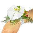 A delicate wrist corsage sits gently on a fair-skinned wrist, placed against a pristine white background so every soft detail reads plainly. The centerpiece is a single large white Phalaenopsis orchid - its broad, satiny petals unfurling like a small, elegant sail - and the lip of the bloom shows a warm splash of bright yellow edged with deeper orange, drawing the eye to the flower's sculpted throat. Beneath and around the orchid, feathery asparagus-fern fronds create a light, lace-like cushion of vivid green that contrasts with the orchid's pure white surface and gives the composition airy movement. To one side a cluster of glossy Hypericum berries nests against the fern; each berry shifts through a gentle gradient from pale green to soft rose and on to a rich cranberry, suggesting a late-summer to autumn palette and adding a small, tactile counterpoint to the smooth petal. Tucked near the berries, ruffled lime-green accent foliage introduces an extra note of texture and brightness so the whole piece reads multi-dimensional. The arrangement is secured to the wrist with a classic multi-strand bracelet of small, lustrous white pearls that curve comfortably and quietly around the skin, lending a touch of heirloom glamour. Soft, natural light reveals glossy highlights on the orchid and the gentle sheen of the pearls; if you close your eyes you might imagine the faint, clean scent of the orchid and cut greenery. This refined corsage, hand-assembled with careful craft, is ideal for weddings, proms or any formal occasion where understated romance is desired - a piece many clients choose after visiting shops near Epping High Street or taking a quiet walk through Epping Forest to choose their wedding flowers.