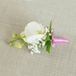 A delicate white orchid boutonniere lies horizontally on a pale oatmeal linen cloth, its woven texture softly visible beneath the flowers, as if carefully set down on a dressing table in a quiet Epping home just before a wedding. At the centre, a single Phalaenopsis orchid bloom opens in pristine white, its broad, velvety petals curving like porcelain wings around a finely detailed throat of soft yellow and the faintest blush of pale pink. Clustered tightly at the base of the orchid, tiny cloud-like tufts of white baby's breath create a halo of airy, romantic texture, each minute bloom forming a gentle contrast against the smooth orchid petals. Slender, vibrant green leaves peek out from behind, adding a fresh, natural accent that hints at gardens around Epping High Street in spring. To one side, a small side stem holds a pair of lime-green orchid buds, still closed and slightly glossy, suggesting new life and blooms yet to come. The stems are neatly wrapped in a bright fuchsia satin ribbon, gathered snugly and tied into a small, elegant bow, its sheen catching the light and lending a joyful pop of colour against the neutral fabric. Gentle, even lighting emphasizes each texture-the satiny orchid, the feathery baby's breath, and the subtle weave of the linen-creating a calm, intimate mood. The overall impression is of a refined, timeless boutonniere or corsage, suited to a groom, bridesmaid, or prom guest in Epping, ready to be pinned on before a ceremony at a local church or a reception in the nearby countryside.