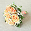 There's a quiet, understated magic to this bridal bouquet: creamy peach roses nestle close together at its heart while a froth of white gypsophila drifts around them like first light. The roses' petals spiral outward with a soft, creamy luminosity that invites touch, and the tiny baby's breath blossoms disperse highlights across the arrangement, lending a soft-focus, ethereal quality. Polished green foliage punctuates the composition, its glossy blades offering a cool contrast that keeps the peach tones vivid rather than dulled. The stems are wrapped in a peach satin ribbon, the finish edged with a string of classic pearls that glimmer when they catch the sun-an elegant, traditional detail that grounds the bouquet in timeless bridal style. In the hand the bouquet feels both light and substantial; the texture is velvety where the roses bloom, feathery where the gypsophila breathes, and smoothly satin at the grip. The scent is understated: a gentle rose perfume with a clean freshness like sheets hung out to dry on a bright morning. As a florist with experience delivering across Epping-from High Street weddings to small ceremonies near the edge of Epping Forest-I know this piece travels well and photographs with soft warmth. At Flowers Epping we often create similar arrangements for brides seeking romance without fuss; it suits a church service, a garden celebration, or an intimate registry gathering, always lending a sense of poised tenderness and hopeful light to the occasion.