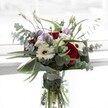 Created by the skilled florists of Flowers Epping, this bouquet captures the essence of celebration and harmony so often found around Epping's village greens and market days. At center stage, lush red roses bloom in deep, velvety layers, lighting up the heart of the arrangement with heartfelt vibrancy. Each rose finds balance with generous white gerbera daisies, whose creamy petals and chocolate centers exude classic charm reminiscent of a sunlit English garden. Sprigs of pale lilac lisianthus meander throughout, their buds hinting at new stories yet to begin-ideal for expressing gratitude or congratulations. Airy white filler flowers and tufts of silvery eucalyptus lift the bouquet, their subtle texture and calming scent intermingling with a sense of pure freshness. A collar of broad, dark leaves provides a sculpted cushion, wrapping the stems in an embracing, elegant frame. The clear vase showcases vibrant, healthy stems glistening beneath the water, echoing the natural vitality of Epping's countryside. Perfect for same-day delivery throughout the town and neighboring villages, this bouquet melds softness with confidence-its appeal universal, yet unmistakably local. Whether brightening a dining table or comforting a neighbor, every bloom tells a story of careful selection and community pride, inviting the senses to linger and savor every petal and fragrance.