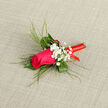 This image shows an elegant boutonnière built around a single magenta-pink rose, carefully shaped and full of life, its petals spiralling in tight layers that invite a closer look. Surrounding the rose are arcs of slender green blades and fine, textural foliage, fanning out like brushstrokes and giving the design both structure and a relaxed, natural rhythm, reminiscent of the greenery edging the paths around Epping Forest. Small sprays of white gypsophila are tucked in at the sides, each spray made up of dozens of tiny, pearl-like blossoms that soften the strong colour of the rose and lend an air of classic romance. The stem is neatly bound with a bright red ribbon, wound in smooth, even coils so that no rough edges show, adding a polished, formal touch. The ribbon's bold crimson tone plays beautifully against the pink and green, hinting at celebration-perhaps a wedding at a local Epping venue, a civil ceremony at the registry office, or a school prom. The boutonnière is photographed against a neutral, slightly textured background that allows every detail to stand out: the subtle gloss on the rose petals, the matte finish of the greenery, and the satin sheen of the ribbon. It feels intimate and personal, something meant to be pinned carefully to a lapel and worn close to the heart throughout the day. The design suggests freshness, individuality, and the quiet confidence that comes from wearing flowers chosen and crafted with intention by an experienced florist in the Epping community.