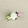 Laid gently on a neutral, lightly textured textile, this elegant boutonniere looks as though it has just been prepared in a calm Epping florist's studio moments before a wedding. At its heart is a fully opened white lisianthus, its petals creamy and soft, unfurling in gentle waves that give the bloom a plush, almost velvety presence. The flower's centre is nestled deep within those ruffled layers, creating a sense of depth and tender abundance. Flanking the main bloom are two creamy lisianthus buds, slim and elongated, one tipped with the faintest hint of opening, the other tightly closed, together suggesting new beginnings and quiet anticipation. Wisps of baby's breath weave between them, their tiny white flowers sprinkling lightness and an airy, romantic texture. Slender green stems and feathery foliage extend gracefully from the side and back, their delicate curves hinting at natural movement, like stems gently stirred by a breeze along Epping High Street. The stems of the boutonniere are carefully bound in a bright pink satin ribbon that gleams softly, wrapped smoothly and secured with a tidy bow at the front. The ribbon's vivid colour adds a modern, joyful twist, standing out against the calm whites and greens without overshadowing them. The soft, even lighting in the scene enhances the sense of tranquillity, emphasising the clean contours and subtle shadows of each petal and leaf. This boutonniere feels perfect for a wedding, prom, or special celebration in Epping, a refined floral detail that carries with it both grace and a hint of playful charm.