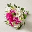 A captivating bridal bouquet is artfully displayed against a light beige background, echoing the refined charm of Epping's floral traditions. At its centre, generous peonies in deep fuchsia burst with layered, ruffled petals, creating a dramatic pop of colour and sumptuous texture. They are beautifully interlaced with clusters of white alstroemeria, each blossom bearing slender, trumpet-shaped petals delicately brushed with maroon streaks-a detail reminiscent of the wild alstroemeria sometimes seen along the paths near Epping Forest. Accents of vibrant green buds stand tall among the blooms, lending both height and freshness, while delicate, creamy white bell-shaped flowers soften the bouquet's rounded form. Dark green foliage weaves discreetly through the arrangement, grounding the vivid hues and adding a sense of depth. All stems are tightly gathered and finished with a striking pink satin ribbon, making the bouquet ready to accompany any bride or grace a celebratory table at a gathering just off Epping High Street. Each flower in this arrangement has been selected to convey feelings of romance, happiness, and grace-a perfect choice for weddings, spring events, or reminder of Epping's rich garden legacy, lovingly crafted by Flowers Epping's skilled florists.