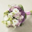 This lush, hand-crafted bouquet rests serenely on a light, subtly textured cloth, its harmonious blend of colour and form celebrating the vibrant spirit of Epping. Large, ruffled white Lisianthus flowers provide a lavish softness, their creamy layers capturing gentle light, while clusters of pastel pink and lavender stock offer a delicate contrast and depth-much like the dappled hues found in Epping's woodland spring blooms. Rising through the arrangement, bold, spiky globes of deep purple Allium 'Star of Persia' supply a modern twist, drawing the eye with their geometric charm and rich tone. Interspersed foliage, from bright green buds to graceful, arching leaves, weaves freshness throughout, infusing the bouquet with a sense of newly gathered vitality. Neatly hand-tied, the stems are enveloped in a pastel fuchsia satin ribbon, its sheen complemented by a line of luminous white pearls-a finishing touch that nods to the understated sophistication of local bridal trends. Soft, even daylight highlights every nuance of texture, from smooth Lisianthus petals to the playful ruffles of the stock and the structural drama of the alliums. Ideal as a wedding bouquet, sophisticated table centerpiece, or a romantic gift for life's milestone celebrations, this floral design from Flowers Epping embodies the artistry and natural elegance beloved by the Epping community-bringing a touch of Essex countryside charm into every special day.